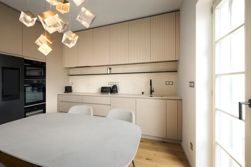 Bespoke kitchen in a matt sand shade with a dining table and a designer pendant light